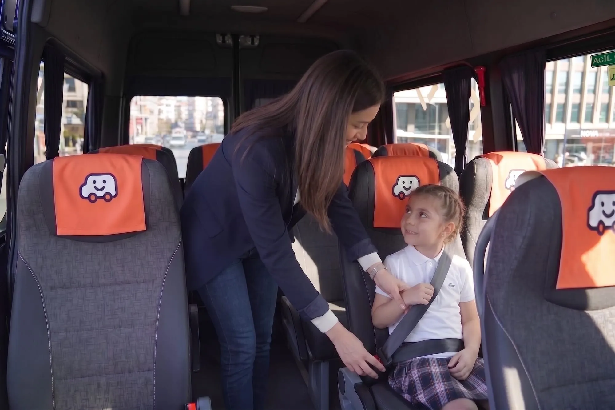 An assistant on the school bus fastening a student's seat belt