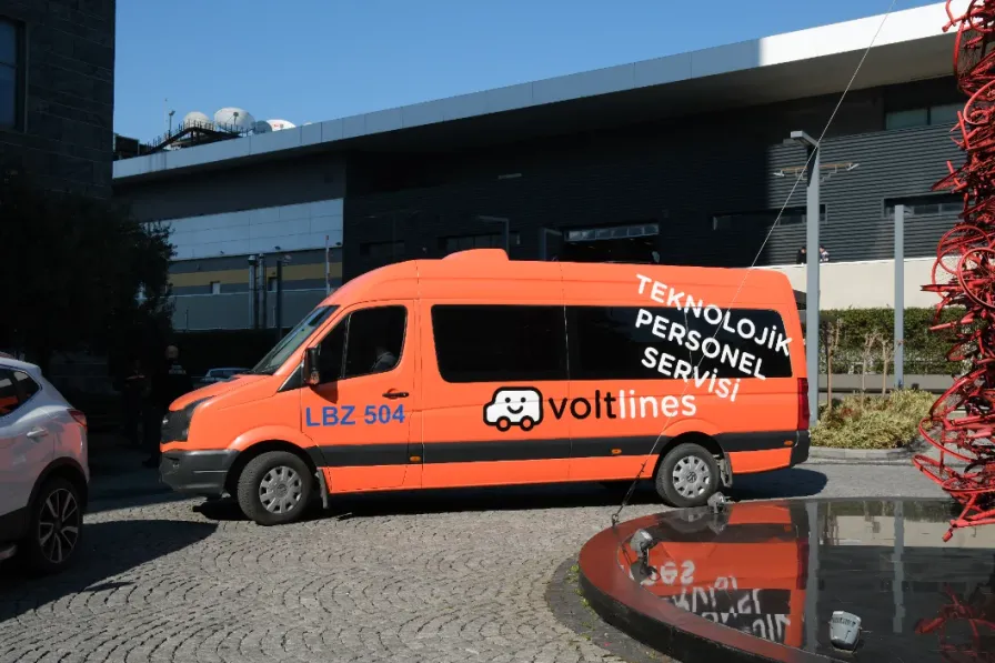 An orange Volt Lines shuttle waiting outside a modern campus building
